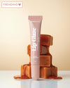 Lip glaze tube with caramel-themed packaging on a beige background