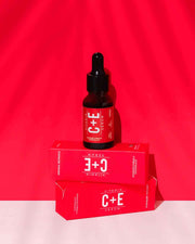 A dropper bottle of Vitamin C & E Serum placed on top of its packaging box, with both items set against a red background.